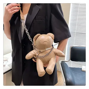 Detailansicht einer beigen Teddybär-Umhängetasche mit Metallkette, getragen von einem Model.