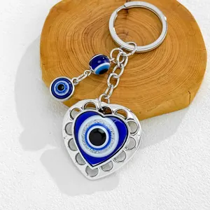 Detailed macro shot of a silver heart-shaped Evil Eye keychain on a wooden base.
