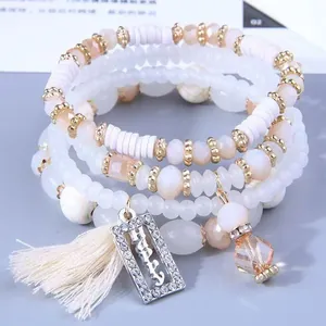 Dettaglio del set di 4 bracciali di perle bianche e champagne con ciondolo Happy e nappe