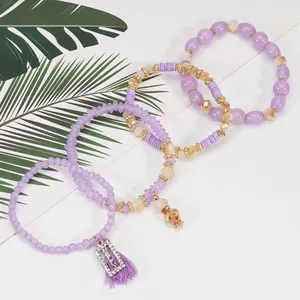 Dettaglio di un set di quattro braccialetti di perle viola con ciondolo happy e nappa