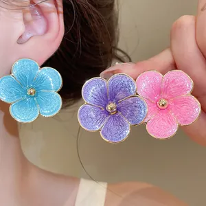 Close-up of vibrant enamel flower stud earrings in blue, purple, and pink