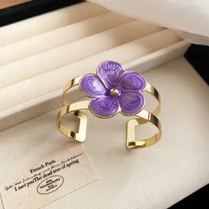 Detailed view of gold cuff bracelet featuring a vibrant purple enamel flower charm