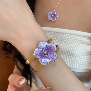 Close-up detail of a purple enamel flower bangle and matching necklace on a female model.