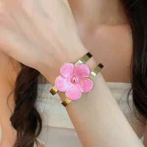 Close-up of elegant gold bangle with pink enamel flower on model's wrist