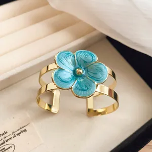 Detailed view of an island style gold cuff bracelet with a vibrant blue enamel flower detail.