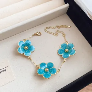 Close-up view of a blue enamel flower bracelet with an elegant gold-plated chain detail