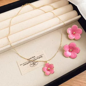Detailed view of a pink enamel flower pendant necklace and matching stud earrings set