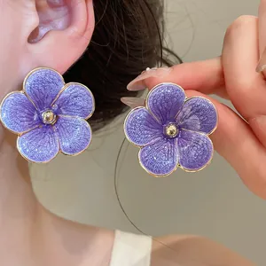 Close-up of elegant purple enamel flower stud earrings with gold trim for a vacation look