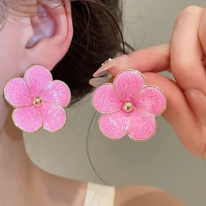 Close-up detail of stylish pink enamel flower stud earrings with textured gold-tone edges
