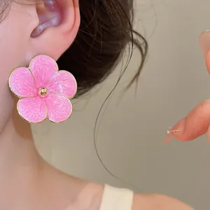 Close-up of a pink enamel flower stud earring with golden rim and textured petals.