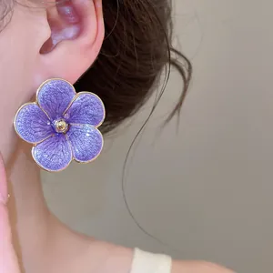 Close-up detail of a purple enamel flower stud earring with gold edges on the ear