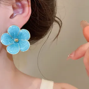 Detailed close-up showing a vibrant blue enamel flower earring worn on a female ear.