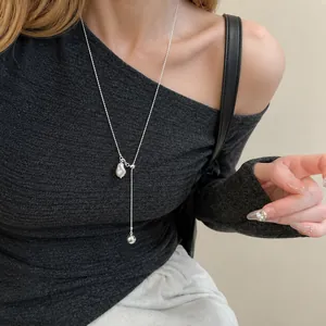 Collana d'argento minimalista con pendenti geometrici e a sfera indossata su un maglione scuro