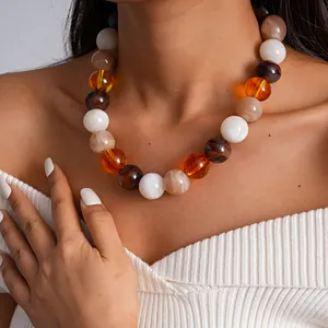 Primer plano de un collar de grandes cuentas de acrílico veteado ámbar y blanco en modelo.