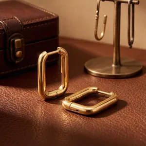 Detailed close-up of gold-plated rectangular hoop earrings on a premium leather surface