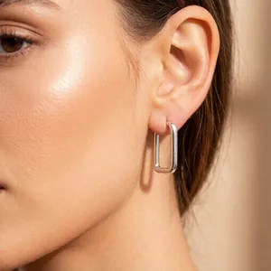 Close-up view of polished silver rectangular hoop earrings worn on a female model's ear
