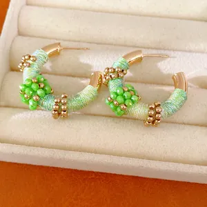 Detalle de pendientes retro en forma de C con tejido de hilo verde y cuentas de cristal