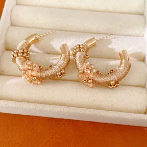 Detalle de pendientes de aro retro en forma de C con cuerda dorada y cuentas finas.