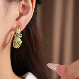 Detalle de un pendiente vintage en forma de C con hilo verde y cuentas en la oreja