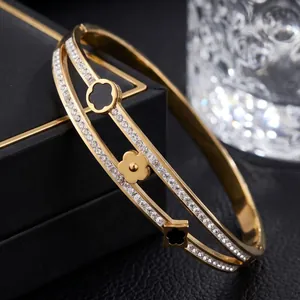 Close-up of elegant double-band gold bangle with lucky clover charms and crystals.