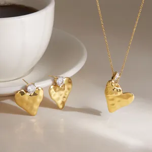 Hammered gold heart pendant and earrings set displayed next to a white coffee cup.