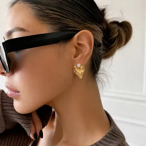 Detailed close-up of a model wearing a textured gold heart stud earring with a sparkling gem