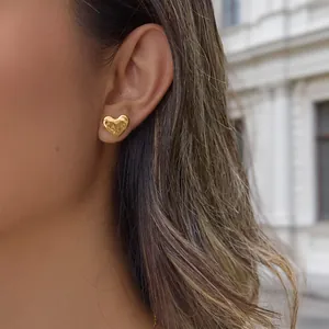 Close-up of a gold-plated heart-shaped stud earring with hammered texture on ear