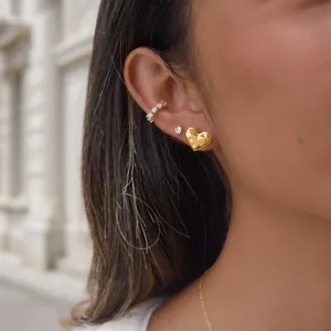 Golden heart stud earring and shimmering crystal ear cuff stacking detail on model