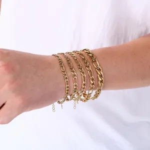 Détail de plusieurs bracelets à maillons Figaro en acier inoxydable doré portés au poignet