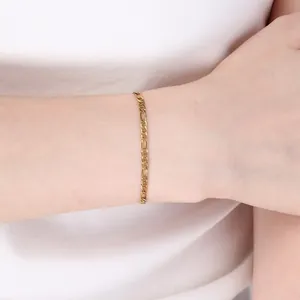 Gros plan d'un bracelet gourmette Figaro en acier inoxydable doré sur un poignet.