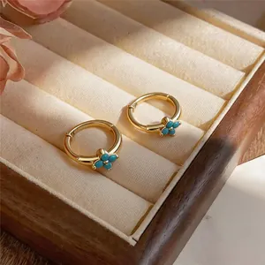 Macro detail view of luxury gold hoop earrings featuring a turquoise four-leaf clover