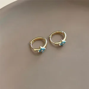 Close-up detail of the turquoise flower setting on gold-toned huggie hoop jewelry pieces.