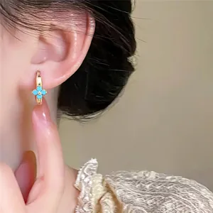 Close-up macro view of a delicate gold-plated flower hoop earring with blue enamel