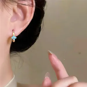Close-up detail of a gold hoop earring featuring a delicate light blue flower charm