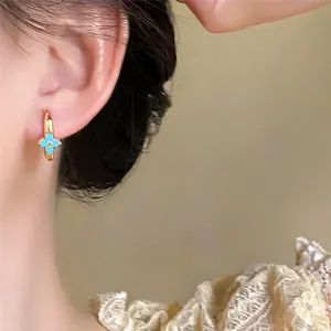 Macro detail view of a gold hoop earring with a light blue clover design on model's ear