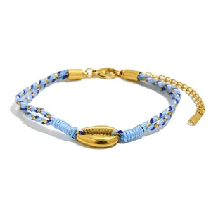 Makroaufnahme eines blau gewebten Armbandes mit poliertem goldfarbenem Kauri-Muschel-Anhänger