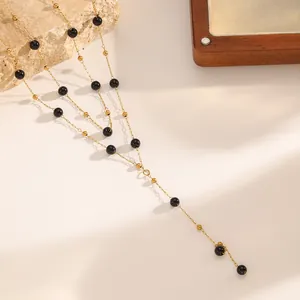 Close-up detail of titanium steel Y-necklace with black and gold beads in warm light