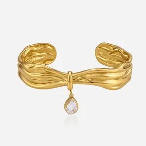 Close-up detail of wavy gold titanium steel cuff bracelet with pear zircon charm