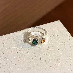 Close-up detail of clear resin ring with embedded green and orange rhinestones