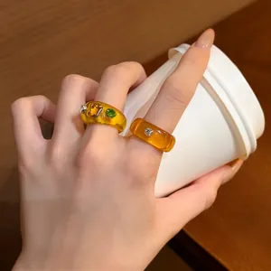 Detailed view of chunky amber resin rings with sparkling rhinestone accents on hand.