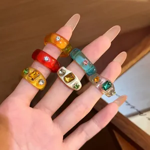 Close-up of colorful resin rings with sparkling rhinestones on a manicured hand