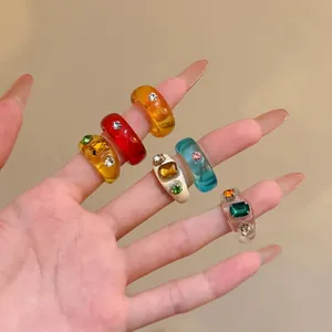Detailed view of colorful resin rings with sparkling inlaid crystals worn on a hand