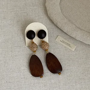 Detail of vintage bohemian earrings with dark wood and straw-woven elements.
