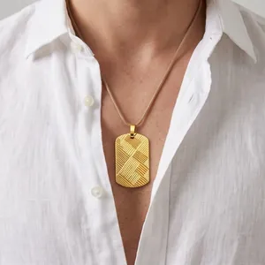 Detailed view of men's gold dog tag pendant with textured diagonal pattern on model