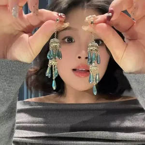 Gros plan de boucles d'oreilles bohèmes en cristal à pompons tenues par un mannequin asiatique.