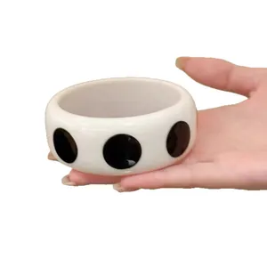 Bracciale rigido in resina bianca a pois neri, tenuto in mano per uno stile minimalista