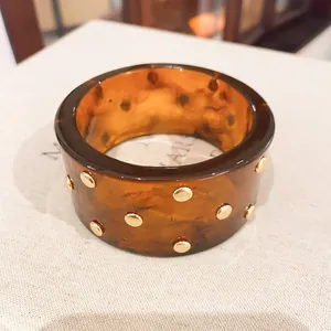 Primo piano del bracciale in resina ambrata marmorizzata con borchie dorate