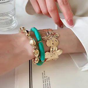 Dettaglio di bracciale in resina marmorizzata verde e polsino floreale dorato al polso