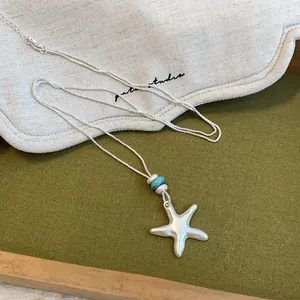 Gros plan du pendentif collier étoile de mer en argent mat avec détails de perles bleues