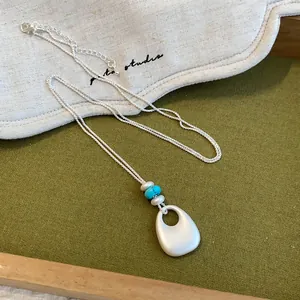 Détail d'un collier en argent mat avec perles turquoise et pendentif goutte d'eau.